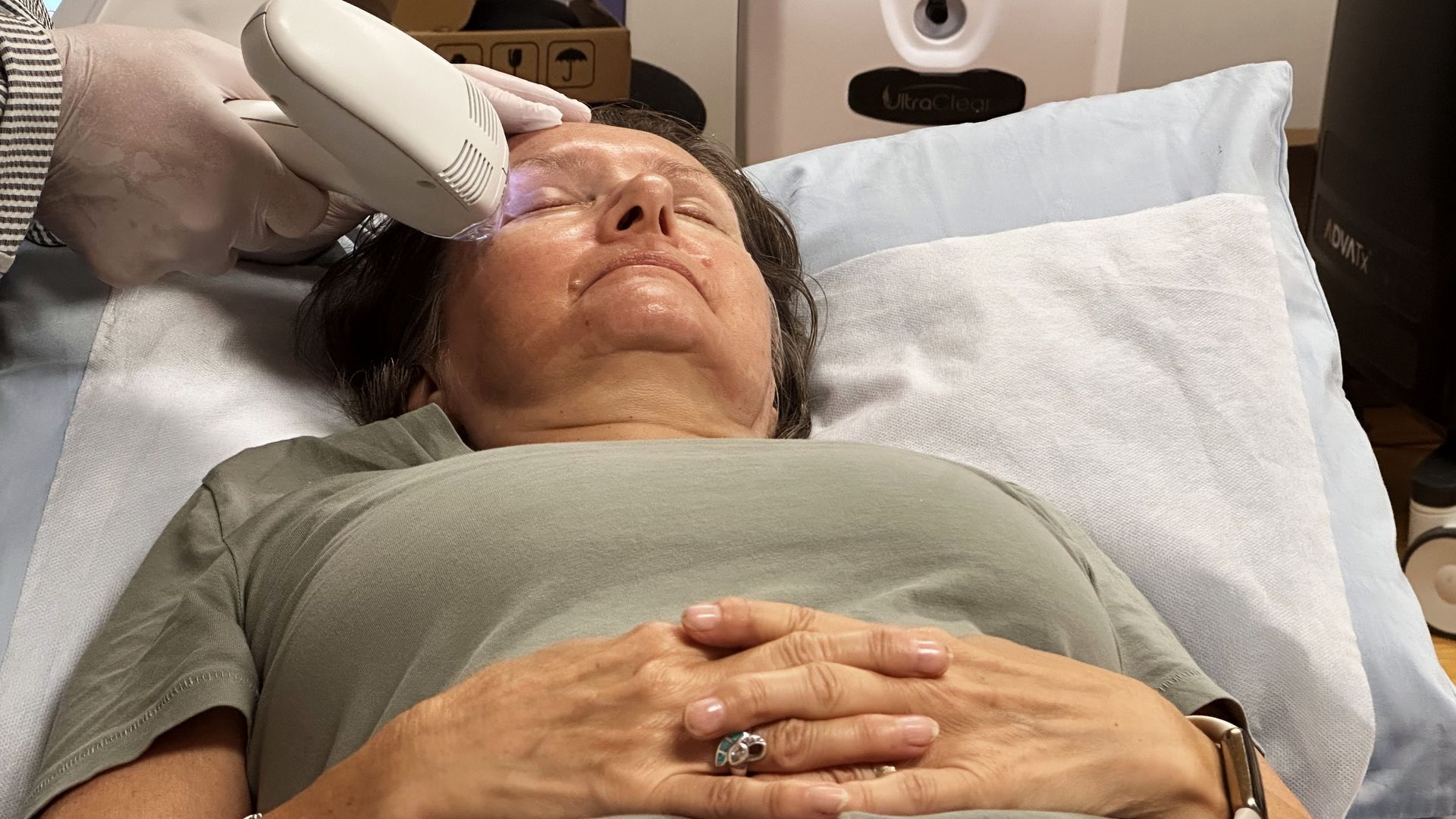 A woman is laying on a bed getting a laser treatment on her face.