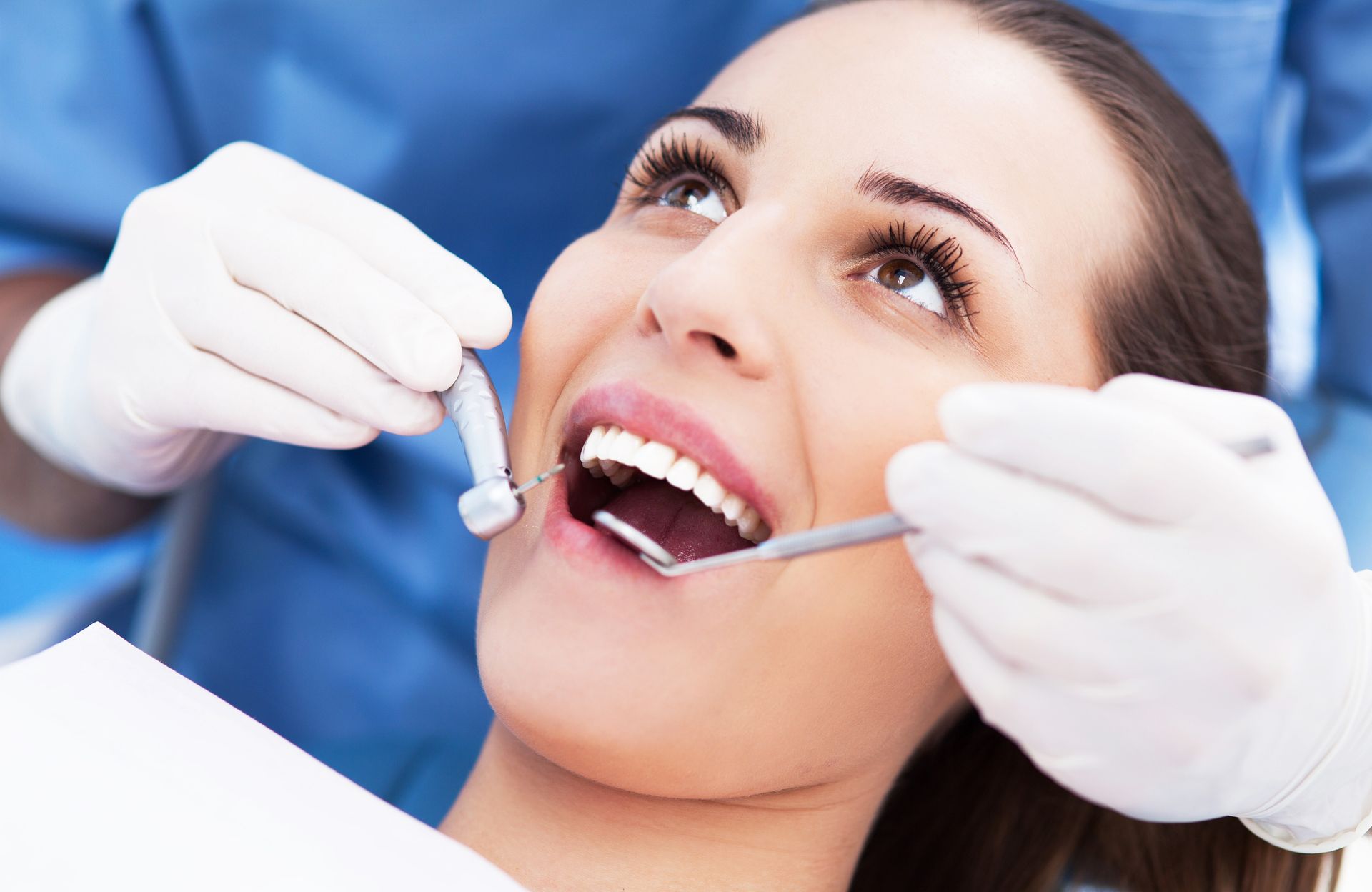 Smiling woman’s teeth being examined by a gloved dentist, showcasing dental clinic services.