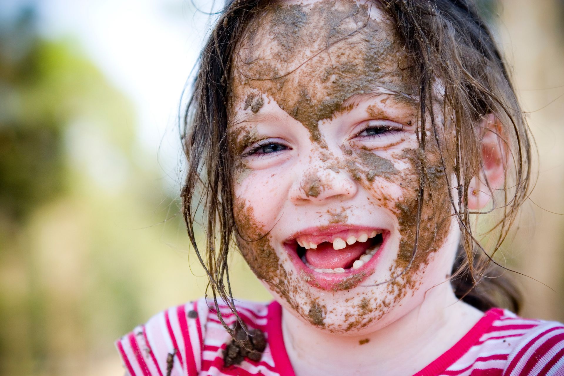 A little girl with mud on her face is smiling.