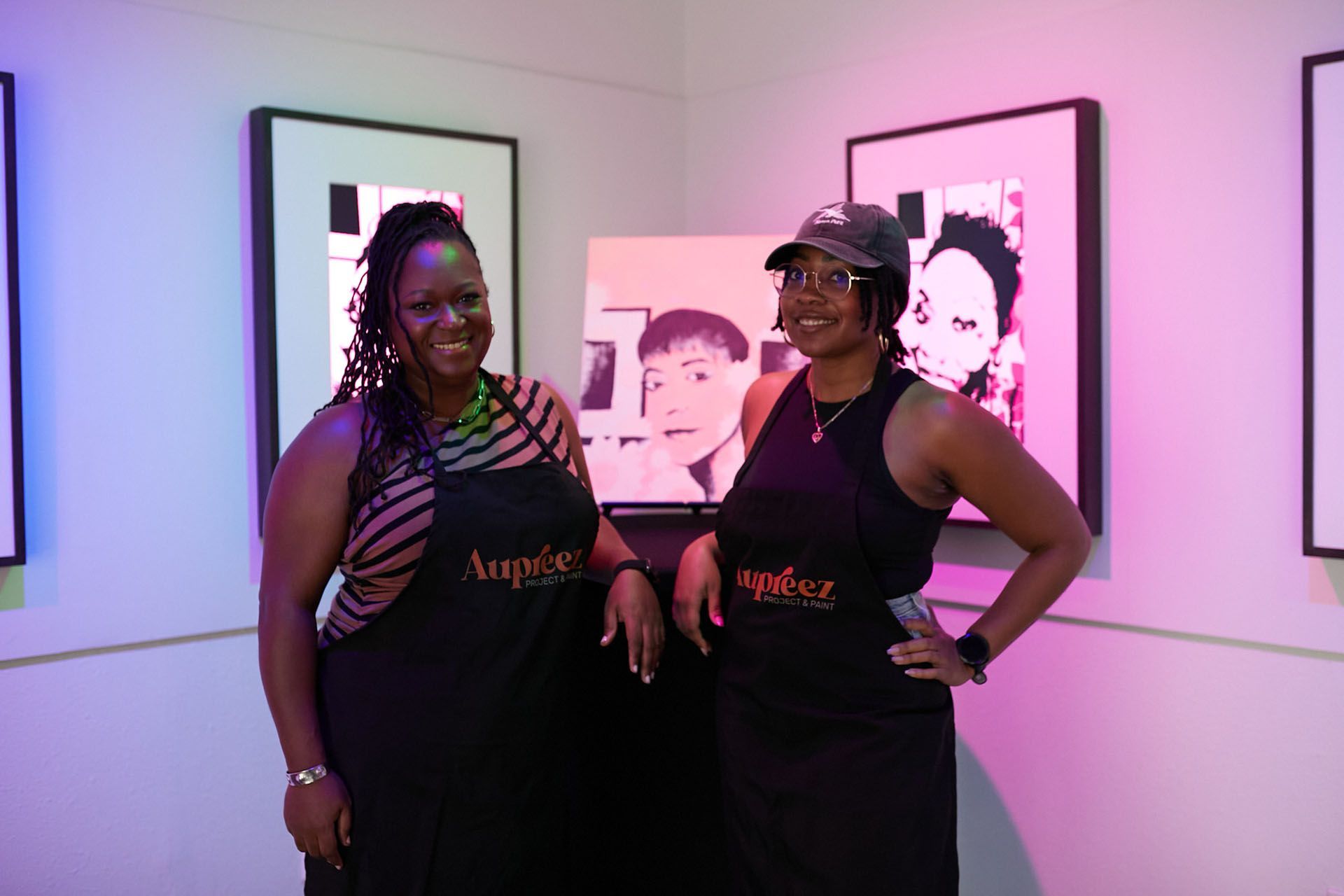 Two women are standing next to each other in front of a painting.