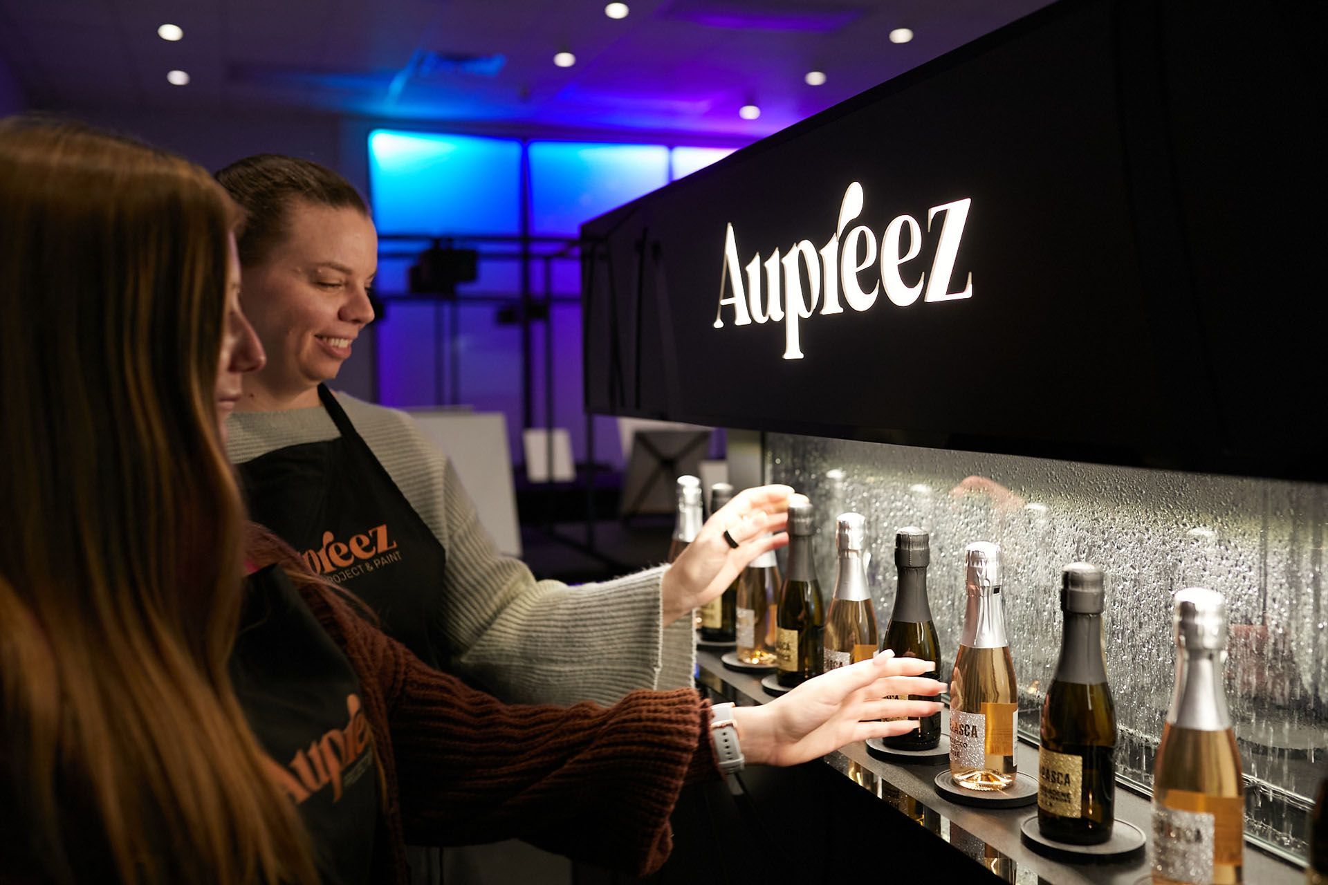 Two women are standing at a bar looking at bottles of champagne.