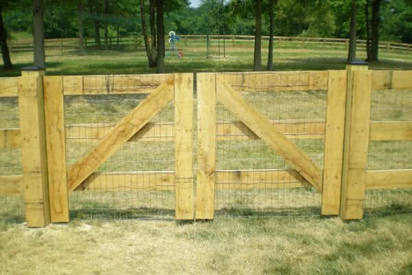 Wooden gate in a grassy field, with a post and rail fence in the background.