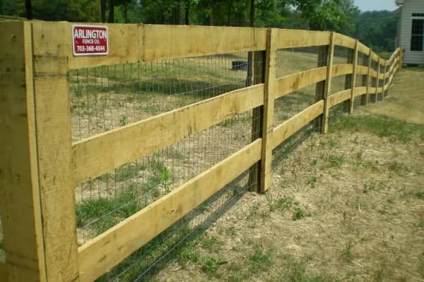 Wooden fence with wire mesh, curving across a grassy field.
