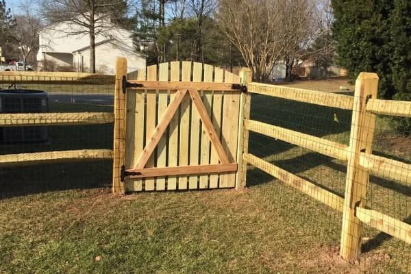 Wooden gate in a split-rail fence; tan and green yard; residential setting.