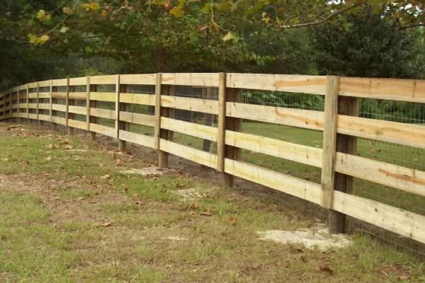 Wooden fence with horizontal rails, surrounding a grassy area.
