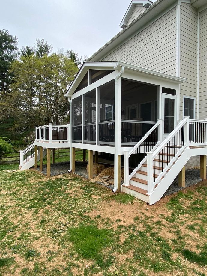 Screened-in porch and deck attached to a house with white trim, black screens, and steps on a grassy hill.
