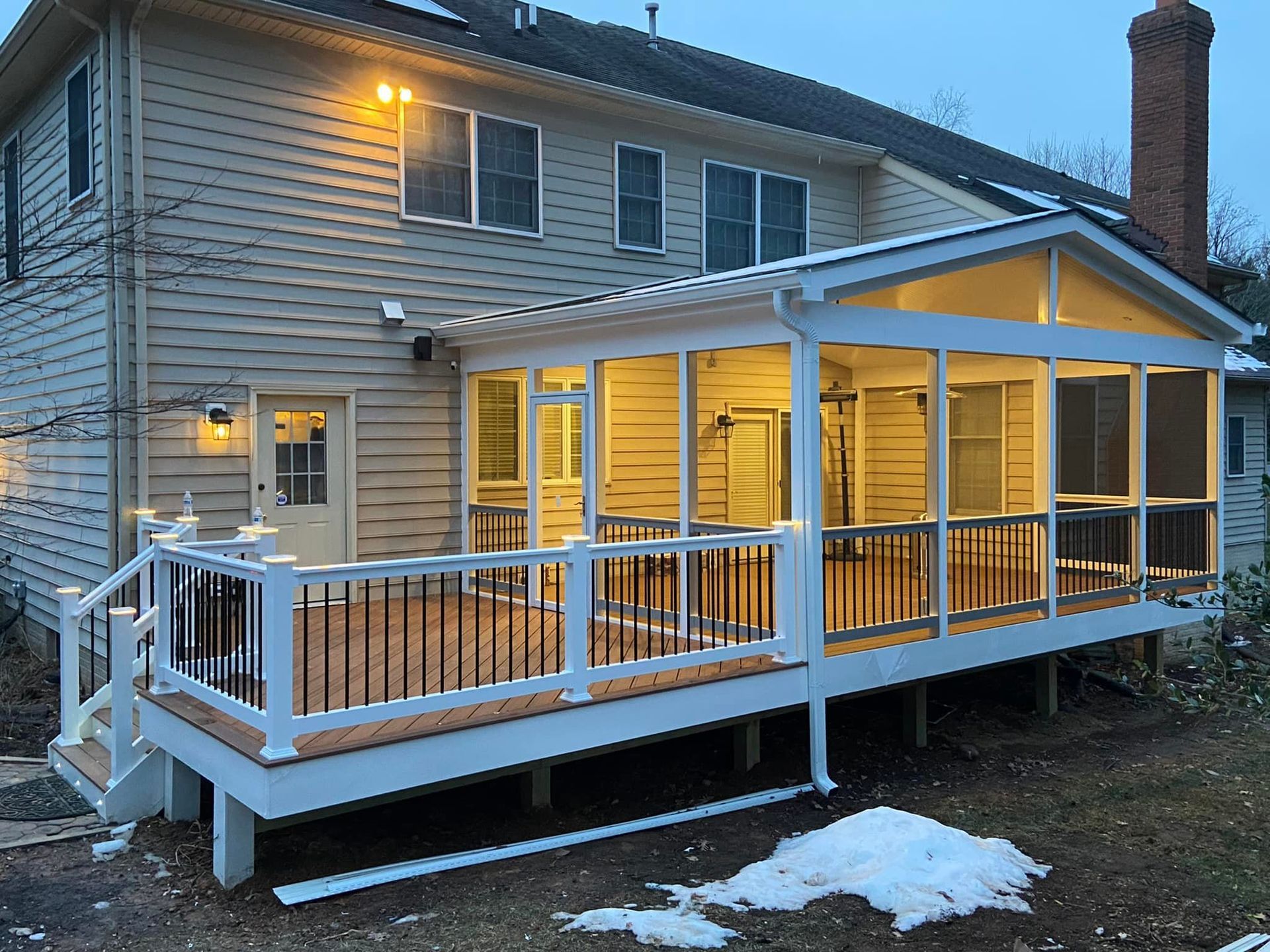 Backyard deck and screened porch extension on a two-story house with snow on the ground.