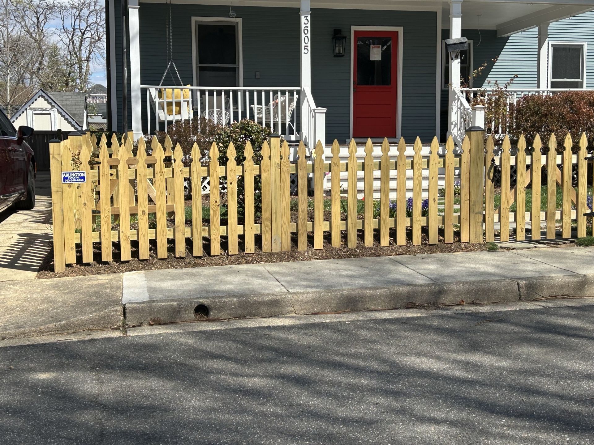 Yellow picket fence in front of a blue house with a red door.