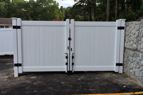 White double gate in a driveway, black hinges and latch, stone wall on the right.