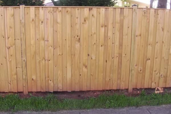 Wooden fence with vertical planks, brown tones, set in a grassy area with a hint of road.