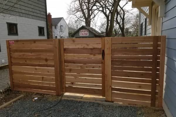 Wooden horizontal slat fence and gate. Exterior view, gravel ground. Light brown wood, black hardware.