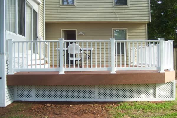 White deck with railing, lattice skirting, brown composite deck boards, and a two-story beige house backdrop.