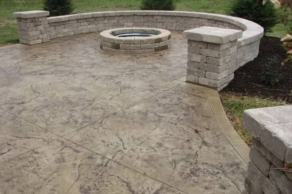 Concrete patio with a circular fire pit and curved stone wall.