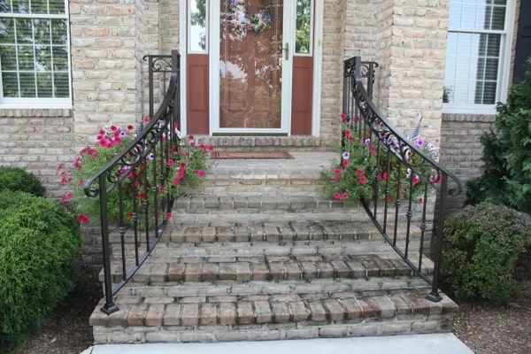 Brick steps leading to a front door with ornate black railings and flower baskets.