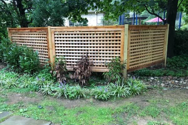 Wooden lattice fence section in a garden, with green plants and grass in front.