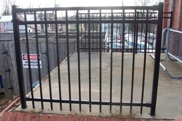 Black metal fence encloses a concrete area near a building with a “Danger” sign.