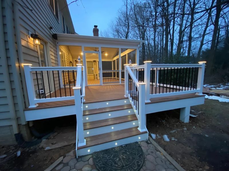 A deck with white railings, black balusters, and built-in lights leads to a screened-in porch, evening.