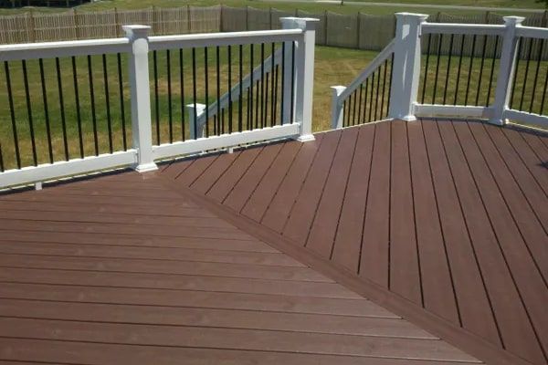 Brown composite deck with white railings, black balusters, and a green yard in the background.