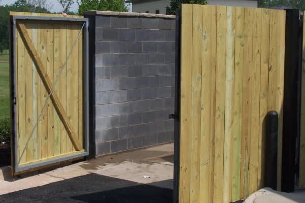 Wooden gate with open panels, framing a cinder block enclosure, asphalt surface.