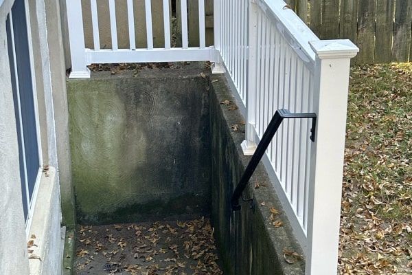 Concrete basement entrance with white railing and black handrail, covered in leaves.