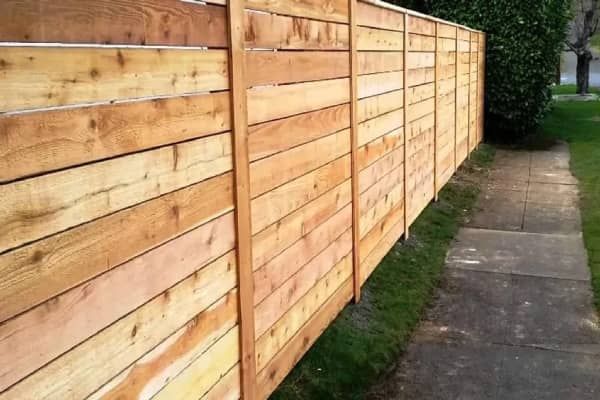 Wooden horizontal fence next to a concrete sidewalk and green grass.