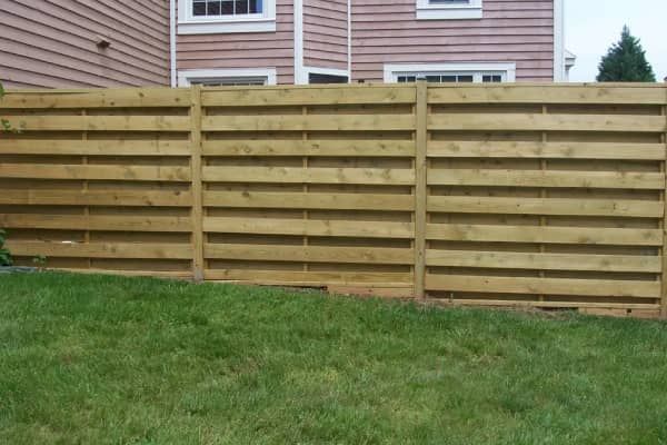 Horizontal wooden fence in front of a house with green grass in the foreground.