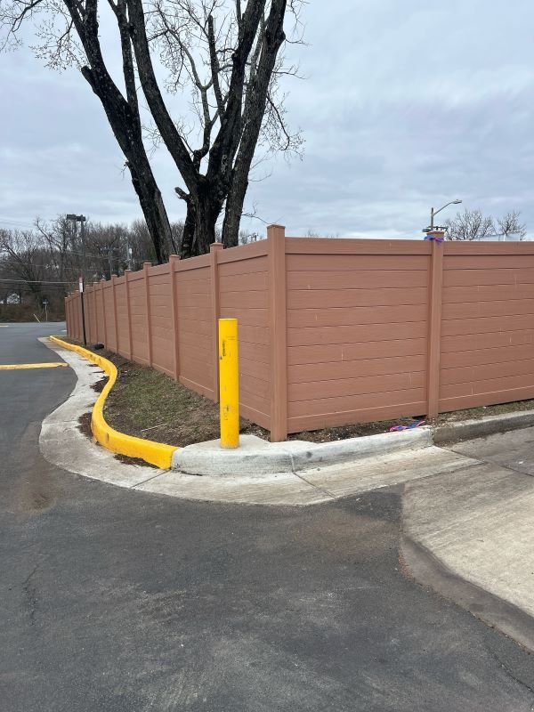 Brown fence bordering a parking area with a yellow bollard post.