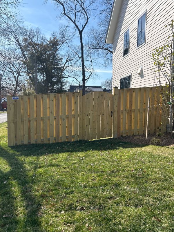 Wooden fence bordering a grassy lawn, adjacent to a house with white siding.