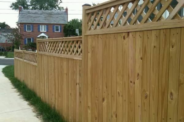 Wooden privacy fence with lattice detail, adjacent to a sidewalk and residential street.