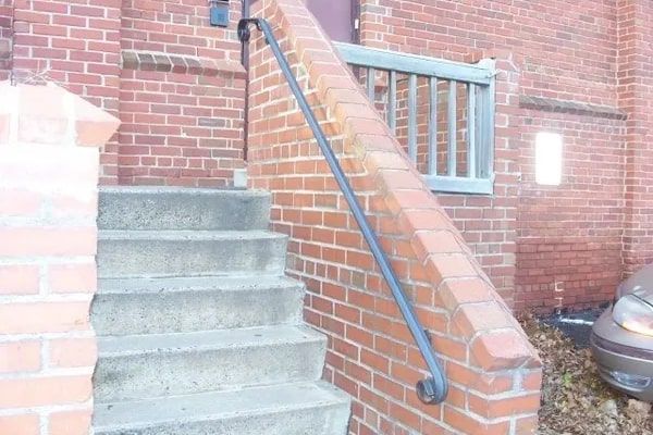 Brick steps with a black handrail leading to a building entrance.