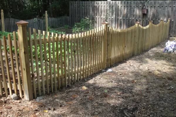 Wooden picket fence surrounding a garden, with a wavy top design.