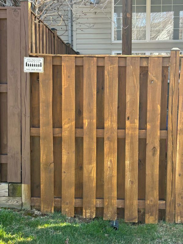 Wooden fence, stained brown, with vertical boards. A small sign is attached. Green grass in foreground.
