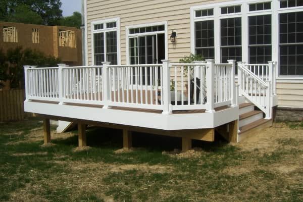 White deck with railing and steps in a backyard setting, next to a beige house with windows.