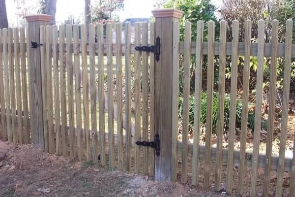 Wooden picket fence with a gate, in a grassy setting.