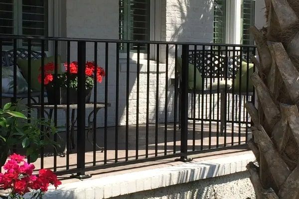 Black metal railing on a porch, with potted flowers and outdoor furniture visible.