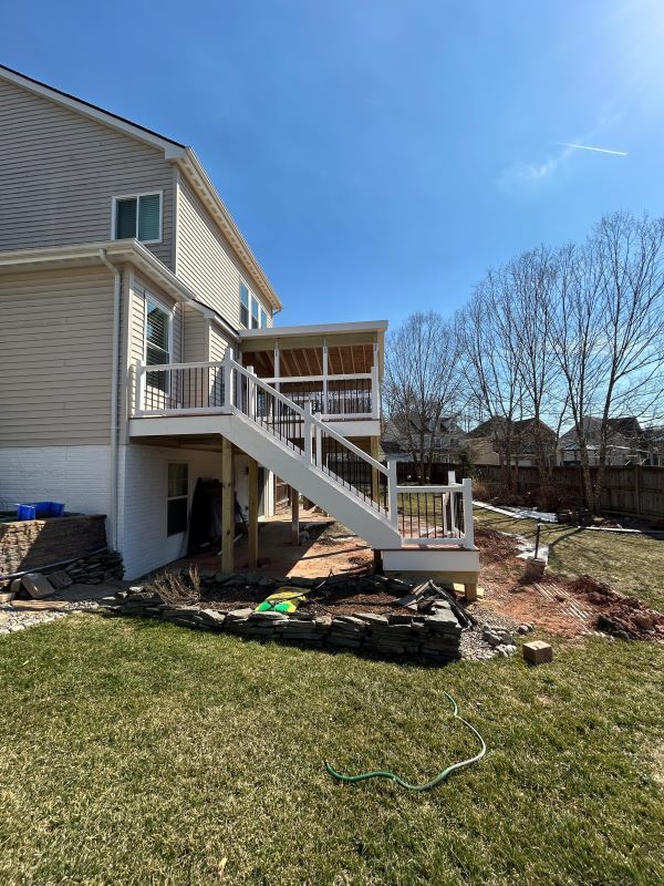 Backyard deck with stairs leading to a covered porch; white railings, tan siding, and green grass.