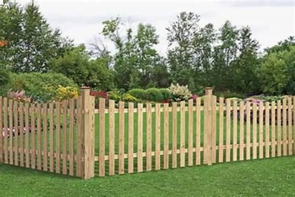 Wooden picket fence surrounding a green lawn and garden with trees in the background.