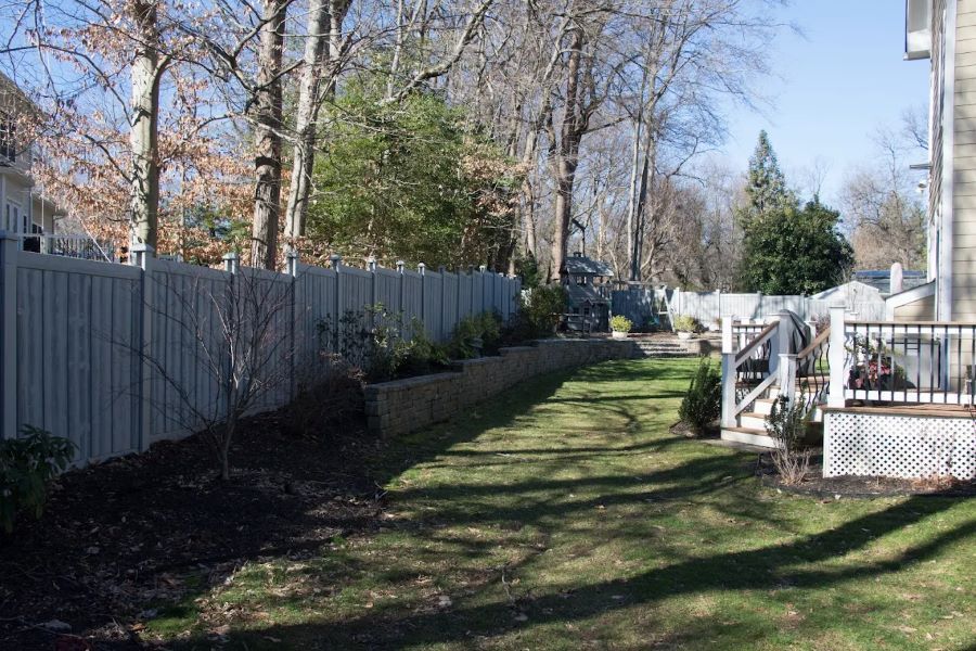 Backyard with a wooden fence, retaining wall, and green grass.