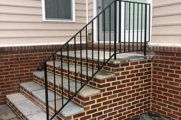 Exterior brick stairs with black metal handrail leading to a door; beige siding above.