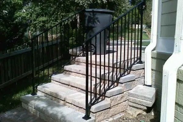 Black metal railing on stone steps leading up to a house, with a trash can at the top.