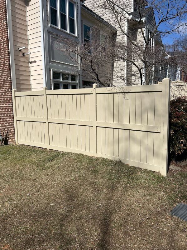 Tan fence in front of a building with brown grass.