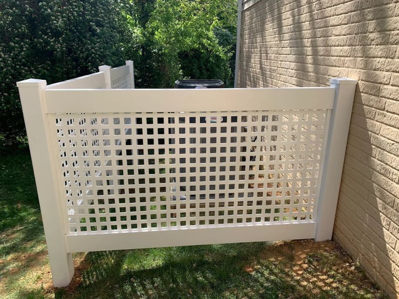 White lattice fence around an air conditioner unit, beside a brick wall, outdoors.