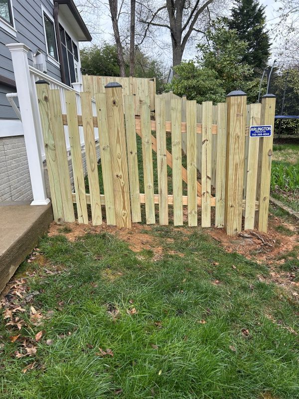 Wooden picket fence with gate in front of a house, set in a patch of grass.