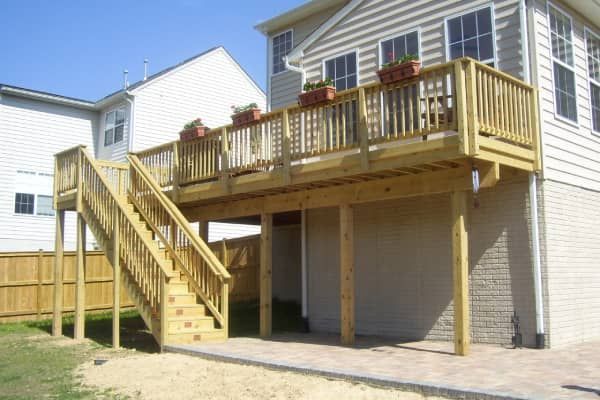 Wooden deck with stairs attached to a house with planters on the railing. Sunny day.
