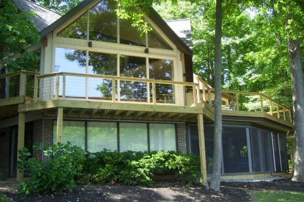 House with large windows and wrap-around deck surrounded by trees.
