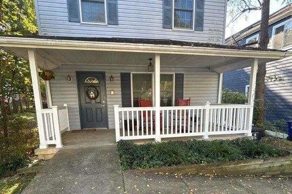 Two-story house with a front porch; white railing and trim. Dark gray door. Sidewalk in front.