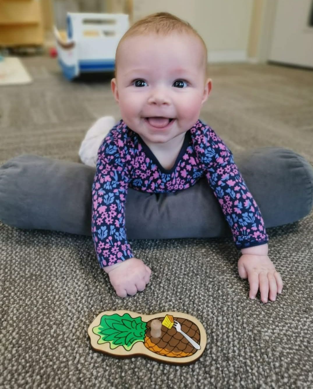 A baby is crawling on the floor next to a wooden peanut puzzle.