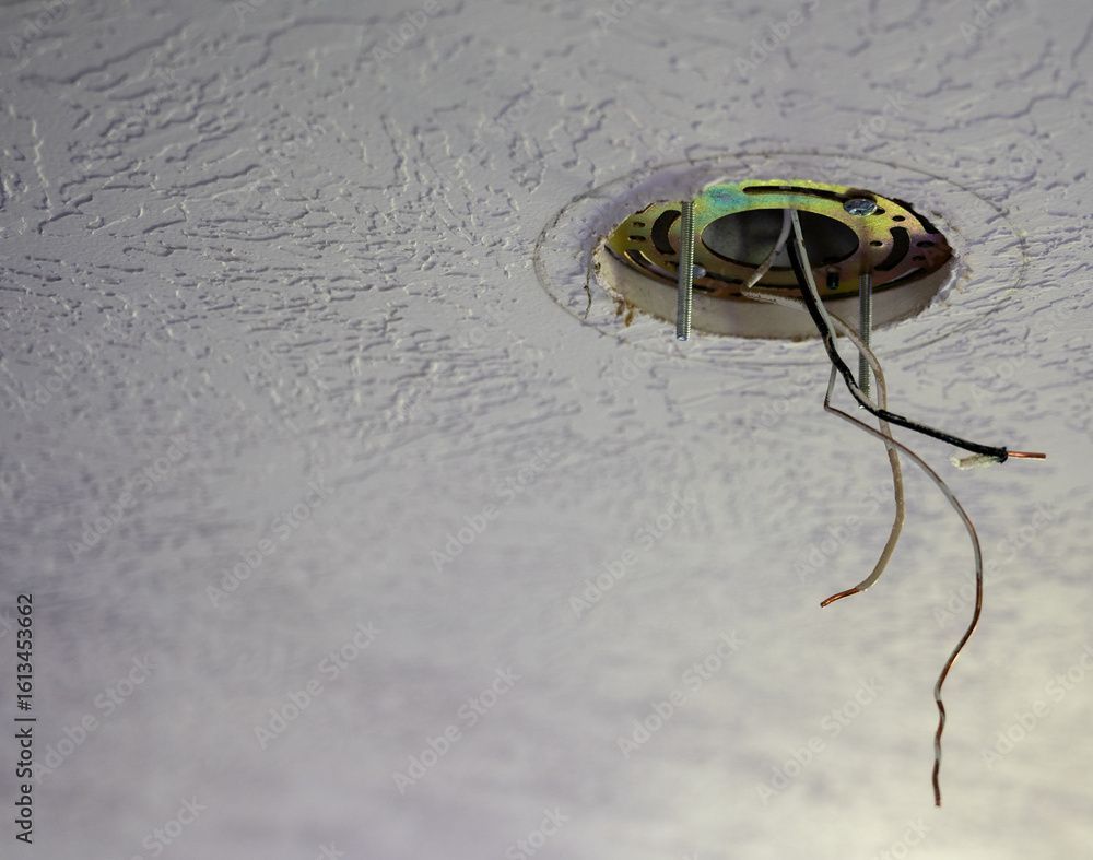 Ceiling light fixture with exposed wires in a textured white ceiling.