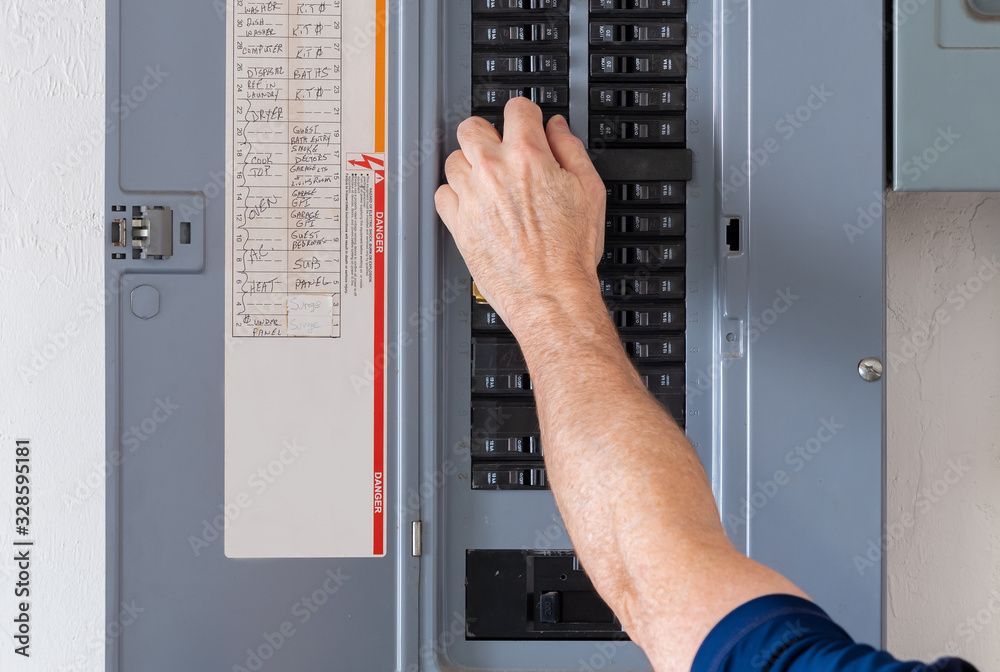 Person's hand flipping a circuit breaker switch in a gray electrical panel.