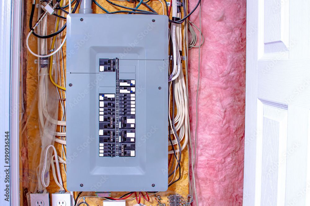 Electrical panel with circuit breakers, surrounded by wires and pink insulation.